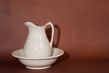 White ceramic pitcher and basin on brown background
