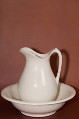 White ceramic pitcher and basin on brown background
