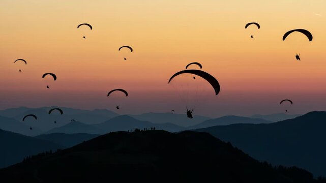 Paragliders silhouetted against a vibrant sunset sky over mountains