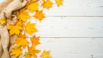 Flat lay of yellow maple leaves and beige fabric on a white wooden surface.