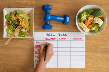 Top view of hand filling meal plan with salad and fresh vegetable. Calories control, meal plan, food diet and weight loss concept.