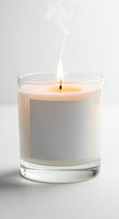A lit candle in a glass jar with a blank label emits smoke against a white background.