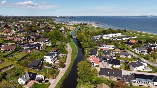 Aerial drone view of Egaa creek winding through a coastal town with houses, greenery, and the sea visible in the distance