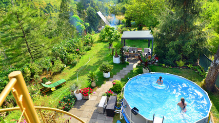 Garden of a suburban house in summer in which you can see a removable swimming pool, pergola in a place with a lot of vegetation.