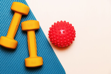 Yellow dumbbells and a red spiky massage ball on a blue yoga mat