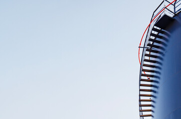 A close-up of dark blue industrial tank with a red safety rail on top, framed against a clear blue...