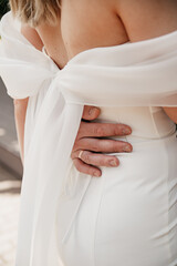 Obraz premium The groom hugs the waist of the bride in a white dress with a slim figure, a gold wedding ring is on his finger