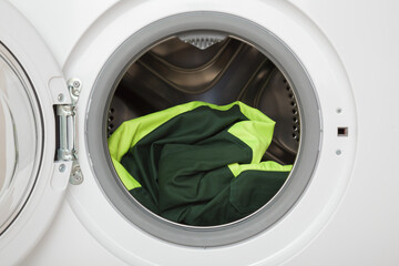 White opened washing machine with dark green workwear with reflective elements. Closeup. Clothes...