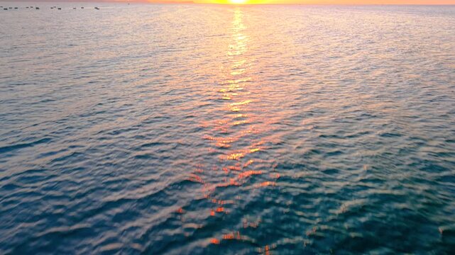 Tilt-up shot from ocean with gentle ripples to golden sunrise sky, clear weather, tranquil seascape glowing in natural light. Royalty high-quality free best stock of the sun rising up