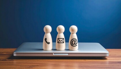 Three wooden figurines with phone, envelope, and @ icons on a laptop—evoking digital connection, communication clarity, and modern outreach.