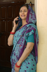 Fototapeta premium Rural indian woman talking on mobile phone standing at village, Use of wireless technology, Digital Technology in india, Mobile banking and Telecom industry. Communication device. Cell phone.