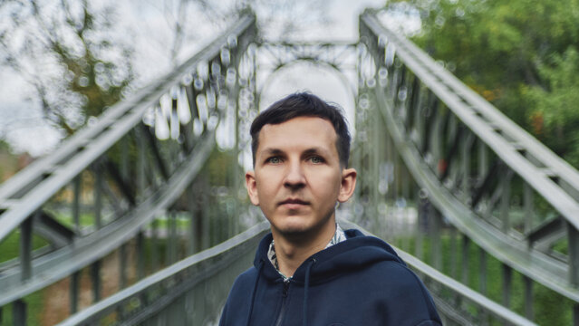 Man stands on a bridge surrounded by greenery on a cloudy day