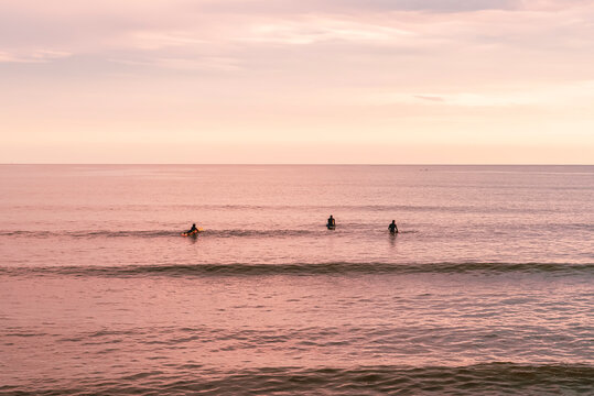 Surfers in the ocean at a pastel sunset