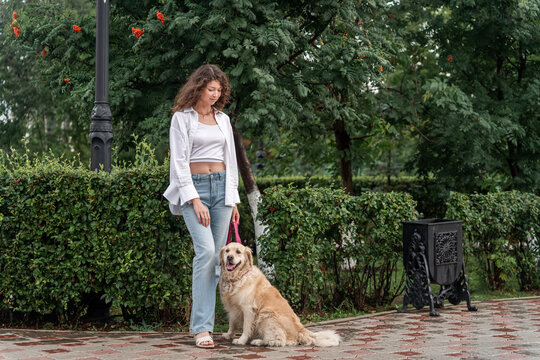 Young woman walking golden retriever on leash in park.