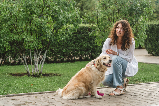 Woman petting golden retriever dog in park. Affectionate moment.