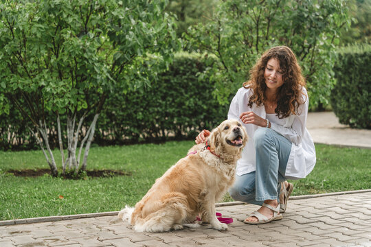 Woman petting golden retriever dog in park. Affectionate moment.