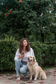 Woman and golden retriever rest in park near rowan tree.