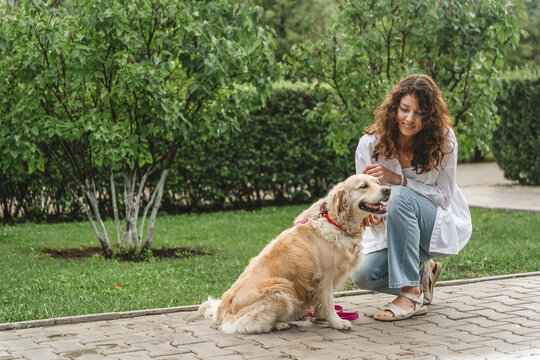 Woman petting golden retriever dog in park. Affectionate moment.