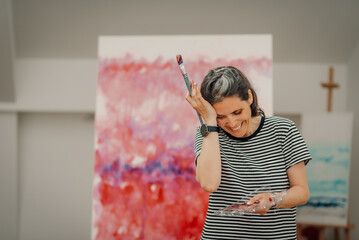 Happy female artist holding paintbrush and palette in art studio