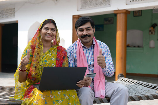 Indian happy rural middle class couple working on laptop in village with debit card