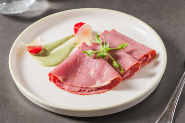 Sliced roast beef with herb sauce and microgreens on white plate