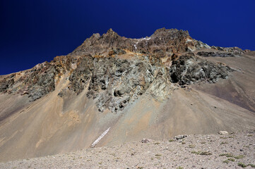 Orange red sand desert, rocky formations and mountains background, blue sky above. Snowy peak against the backdrop of a rocky desert