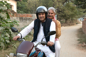 Naklejka premium Happy rural Indian young man with rural father riding on motorcycle