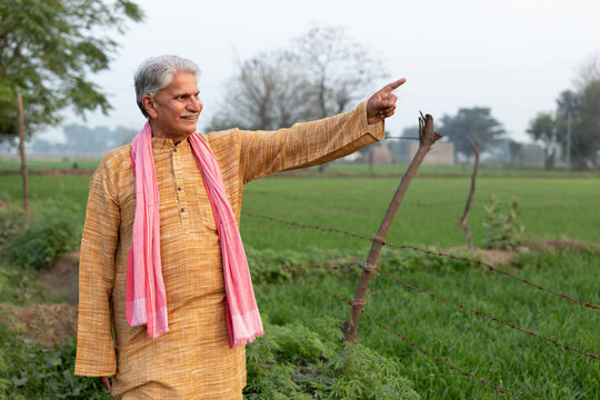 Indian senior rural famer standing in farm, happy farmer pointing finger to side way.