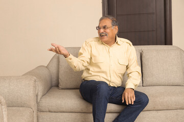 Fototapeta premium Portrait of a indian happy Senior age man sitting at home relaxing on sofa having coffee