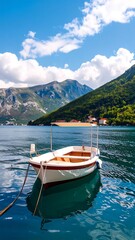 A small white boat floats peacefully on a calm bay, reflecting the vibrant blue water.  Mountains and lush green hills rise in the background, beneath a bright blue sky with puffy clouds