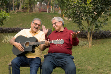 Fototapeta premium Two carefree senior male friends playing guitar and having fun at park