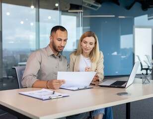 Obraz premium Two Colleagues Discussing Business Strategy with Laptop and Documents in Modern Office