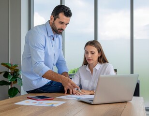 Obraz premium Two Colleagues Discussing Business Strategy with Laptop and Documents in Modern Office