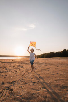 Child running with kite on beach at sunset, vertical with copy space