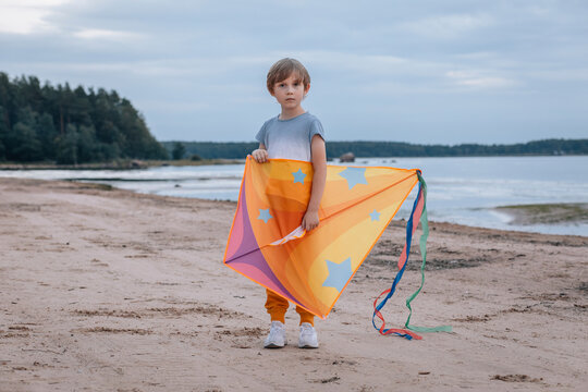 Boy holding bright kite on quiet beach, horizontal with copy space