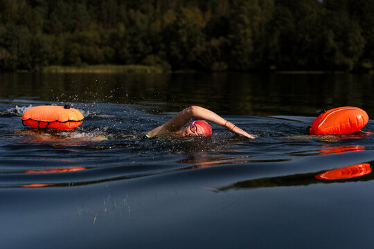 Swimmer in a lake with a safety buoy, wearing a red cap and goggles