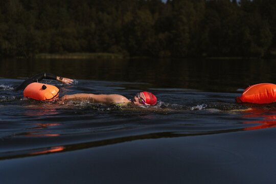 Swimmer in a lake with a safety buoy, wearing a red cap and goggles