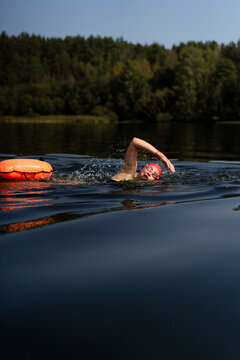 Swimmer in a lake with a safety buoy, wearing a red cap and goggles
