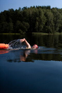 Swimmer in a lake with a safety buoy, wearing a red cap and goggles