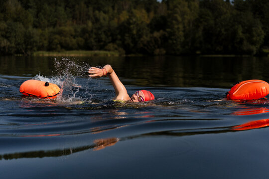 Swimmer in a lake with a safety buoy, wearing a red cap and goggles