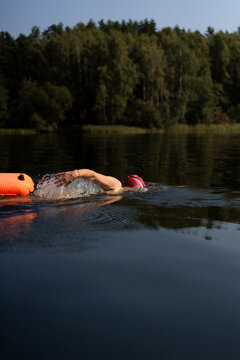 Swimmer in a lake with a safety buoy, wearing a red cap and goggles