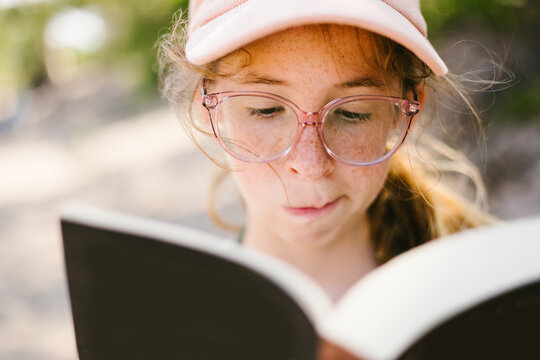 Tween blond girl on beach with glasses and freckles reading a book