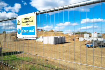 Shallow focus of a Keep Out sign seen attached to a metal fence at the perimeter of a new housing development site in the UK.  Land can be seen being cleared behind the fence.