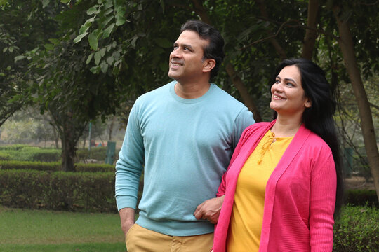 Indian happy young couple standing and looking each other with love and care. Indian Smiling young couple holding hands and standing outdoors at the nature. Celebrate the form of love at park