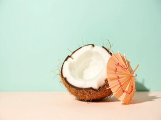 Refreshing summer dessert concept with white sweets or ice cream balls served in half coconut shell decorated with colorful paper umbrellas on pastel background. Minimal and tropical food styling.