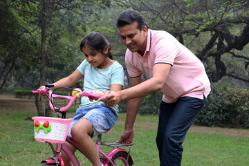 Fototapeta premium Indian Father teaching kid daughter to ride bicycle outdoors in park