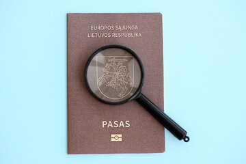 Lithuania passport and magnifying glass on light blue paper. Citizenship details and information