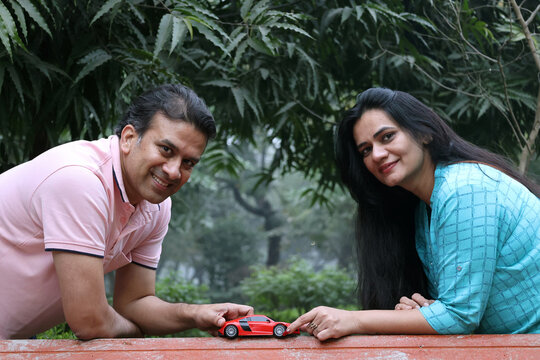 Indian happy cheerful couple holding car model in hand at park. Concept : Car Loan