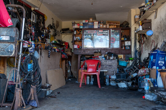 RABAT, MOROCCO - 26 Dec 2023: A dirty, cluttered garage in a developing country with oil-stained floor and walls lined with car parts and storage cupboards.