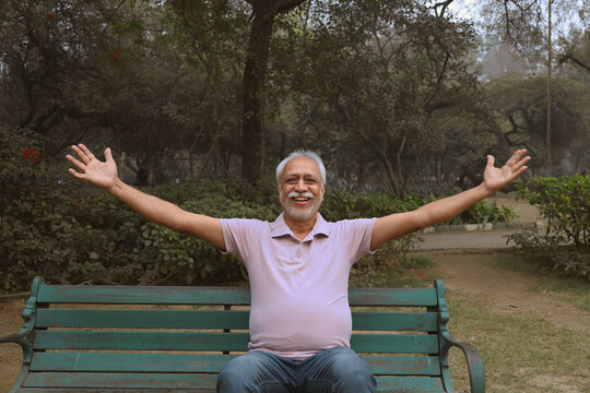 Cheerful senior man spreading hands in autumn park. Wearing light pink half sleeve color t-shirt. Concept of successful, confident healthy senior and wellness, elder enjoying after after retirement